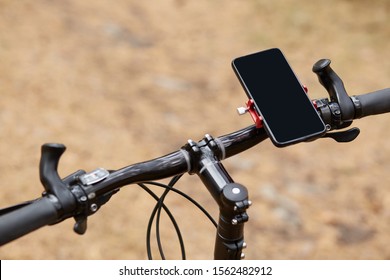 Black handlebar of sport bicycle over forest road background, having smartphone attached to right side, movement along road, gps navigator, going according to online map. Orientation concept.