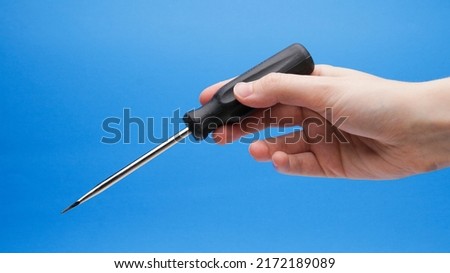 Black Handled Flat Head Screwdriver At Angle In Hand On A Blue Background