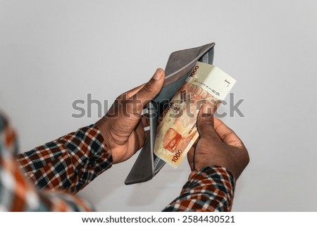 Black hands Holding empty opened men wallet containing single Uganda shilling note. hand removing money out of wallet. no money poor person concept 