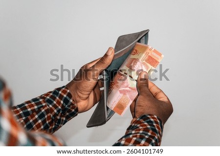 Black hands Holding empty opened men wallet containing single 100000 Indonesian rupiah note. hand removing money out of wallet. no money poor person concept 
