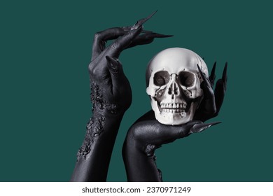 Black hands of witch with skull on green background. Halloween celebration