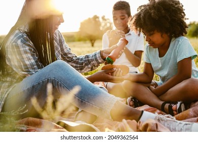 Black Happy Family Eating Hotdogs During Picnic On Summer Field