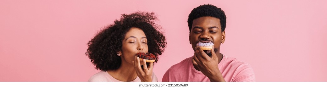 Black happy man and woman having fun and eating donuts isolated over pink background - Powered by Shutterstock