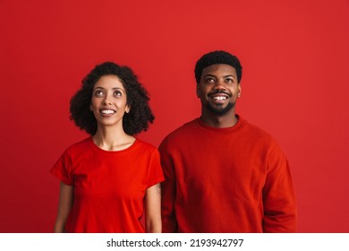 Black Happy Man And Woman Smiling And Looking Upward At Copyspace Isolated Over Red Background