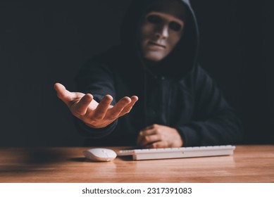 Black hat hacker force demands ransom by holding out his hand on table where sensitive data is hacked in a dark room in the background. Cyber security and cyber crime concept. Hacking and phishing