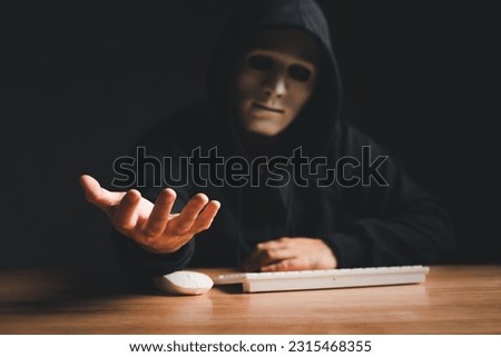 Black hat hacker force demands ransom by holding out his hand on table where sensitive data is hacked in a dark room in the background. Cyber security and cyber crime concept. Hacking and phishing