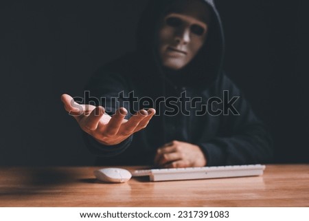 Black hat hacker force demands ransom by holding out his hand on table where sensitive data is hacked in a dark room in the background. Cyber security and cyber crime concept. Hacking and phishing
