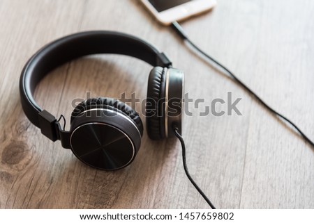 Black headphones and smartphone on wooden background.