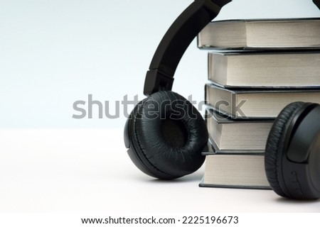 Black headphones with stack of books on light background. Audio books or modern education concept.