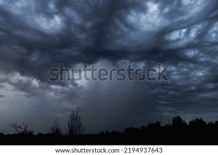 Black, heavy, undulating storm clouds. There is a brighter spot between the unevenness, the gap from which a trail of rain pours out.