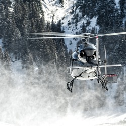 Black Helicopter Departed From A Snowed Altiport With Whites Reflection In The Fuselage. The Rotor's Power Raises The Snow Creating A Dust. It Transport Skiers And Material Above The Mountains.