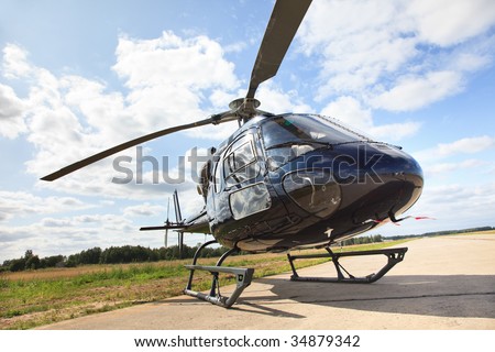 Black helicopter standing on landing strip in airfield. Low angle view with nice cloud reflection.