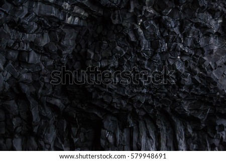 Black hexagonal volcanic rock and columnar basalt formations in the wall of the small cave on the black sand beach at Vik in southern Iceland