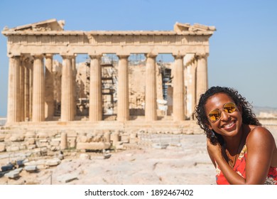 Black Hipster Traveler Smiling Sitting In Ruins, On The Background Of The Parthenon On The Acropolis Of Athens, Greece. Vacation Woman Enjoying The Visit In Athens