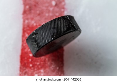 Black Hockey Puck On The Ice Rink, With Painted Red Line.