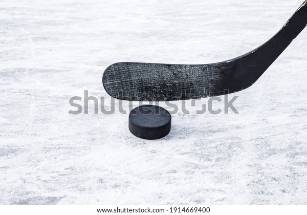 Black hockey stick and rubber puck on ice\
background. Closeup. Front\
view.