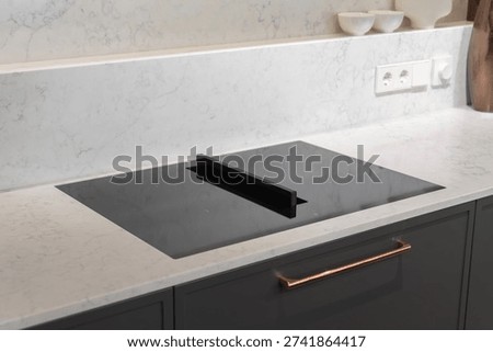 Black induction cooktop with downdraft riser on marble countertop