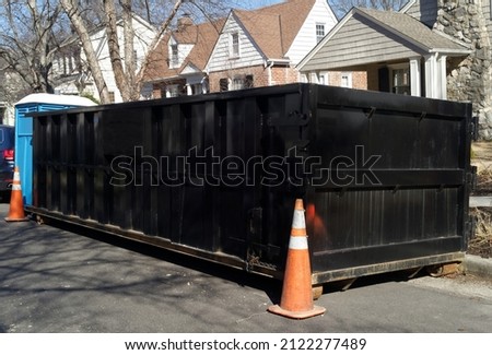 Black industrial dumpster container on neighborhood street. 