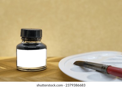 Black ink bottle with empty white label with ink brush and a palette, yellow background, mock up.