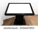 Black interactive touch table with empty blank screen stands in white interior on wooden floor, high-tech mockup