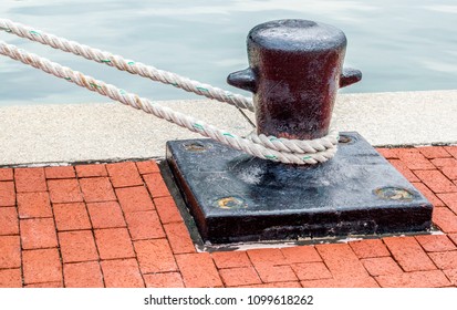 black iron bollard with mooring lines wrapped around it on a red brick walkway in Baltimore's Inner Harbor