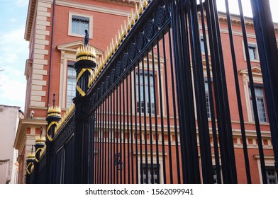Black iron cast gate with golden spearhead and Roman fasces in front of the brick-built building of the Court of Appeals of Toulouse, France (part of the Palace of Justice)