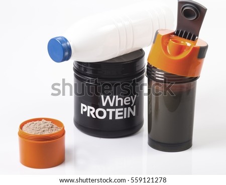 Black jar with whey fitness protein. Bottle with milk on the jar. Shaker with milk near. Orange cup with protein in foreground. Nutrition for fitness and diet. White background.