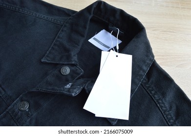 Black jeans denim coat jacket and blank sale tag paper, on wooden floor - Shutterstock ID 2166075009
