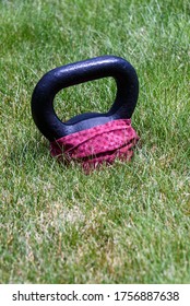 Black Kettle Bell With A Red Face Mask, On A Green Lawn, Ready For An Outdoor Workout
