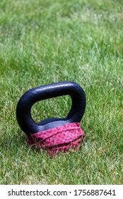 Black Kettle Bell With A Red Face Mask, On A Green Lawn, Ready For An Outdoor Workout
