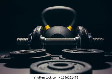 Black kettlebell with yellow marking with free weights and plates in front of it