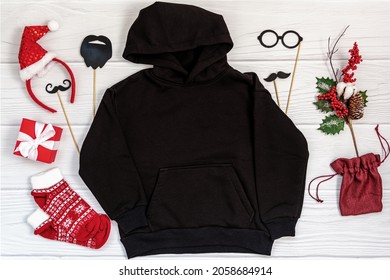 Black kid sweatshirt with a hood on white background top view. Blank flatlay black kids hoodie on white wooden backdrop with christmas props, unisex winter apparel mockup