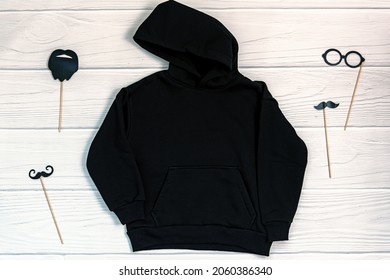 Black Kid Sweatshirt With Hood On White Background Top View. Blank Flat Lay Black Kids Hoodie On White Wooden Backdrop With Christmas Props, Unisex Winter Apparel Mockup