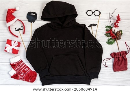 Black kid sweatshirt with a hood on white background top view. Blank flatlay black kids hoodie on white wooden backdrop with christmas props, unisex winter apparel mockup
