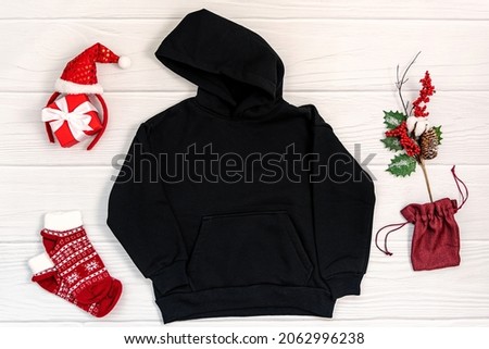 Black kid sweatshirt with a hood on white background top view. Blank flat lay black kids hoodie on white wooden backdrop with christmas props, unisex winter apparel mockup