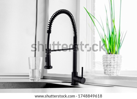 Black kitchen faucet on the silver sink near the glass of water 
