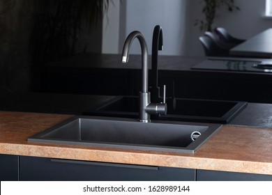 Black Kitchen Sink With A Mixer In A Kitchen With Black Fronts, Black Handles And Black Glossy Backsplash With Copper Look Countertop. 