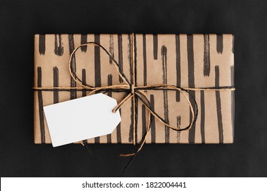 Black And Kraft Christmas Gift With A Blank Tag Mockup On A Black Background.