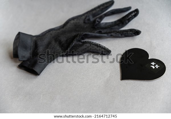 A\
black lace glove and a paper heart against a gray background. A sad\
face with crosses over the eyes is drawn in white marker on the\
heart. Unrequited love, loss of a loved one\
concept.