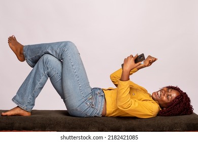 black lady lying on a bench using a phone rejoices