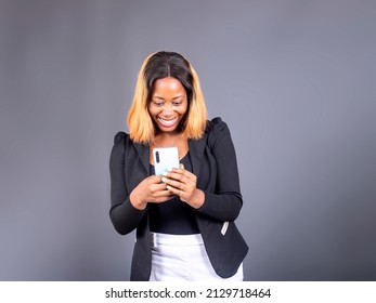 Black Lady Texting On Her Phone Standing Over A Gray Studio Wall Background