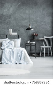 Black Lamp Near Table With Books And Clock In Monochromatic Bedroom Interior With White Chair At Desk With Heather Next To Bed With Knot Pillow