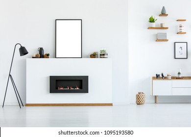 Black Lamp Next To Fireplace In White Living Room Interior With Mockup Of Empty Poster. Real Photo