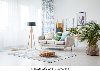 Black lamp standing by a sofa and a row of candles lying on the floor in front of a window shedding light on the interior of boho style living room