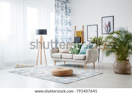 Black lamp standing by a sofa and a row of candles lying on the floor in front of a window shedding light on the interior of boho style living room