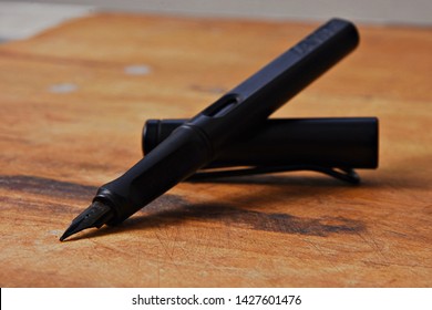 A black Lamy fountain pen resting on a wooden work surface