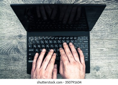 Black Laptop On Wood With Hands Viewed From Above.