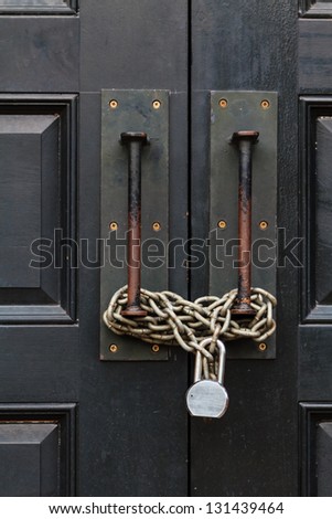A black large door closed with a chain and a lock