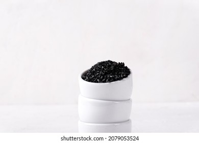 Black lava salt in stack of small bowls on the white table. Copy space