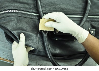 Black Leather Bag cleaning with a Microfiber cloth in a leather factory. The hands of the worker covered with gloves are into sharp focus and no human face is visible in the image.  - Shutterstock ID 509129353